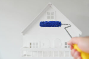 POV (point of view) of a person holding a paint roller brush with blue color against a white house. Renovation, home decoration and painting house concept. No people. Copy space
