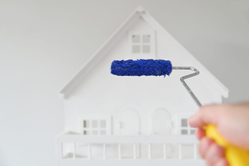 POV (point of view) of a person holding a paint roller brush with blue color against a white house. Renovation, home decoration and painting house concept. No people. Copy space