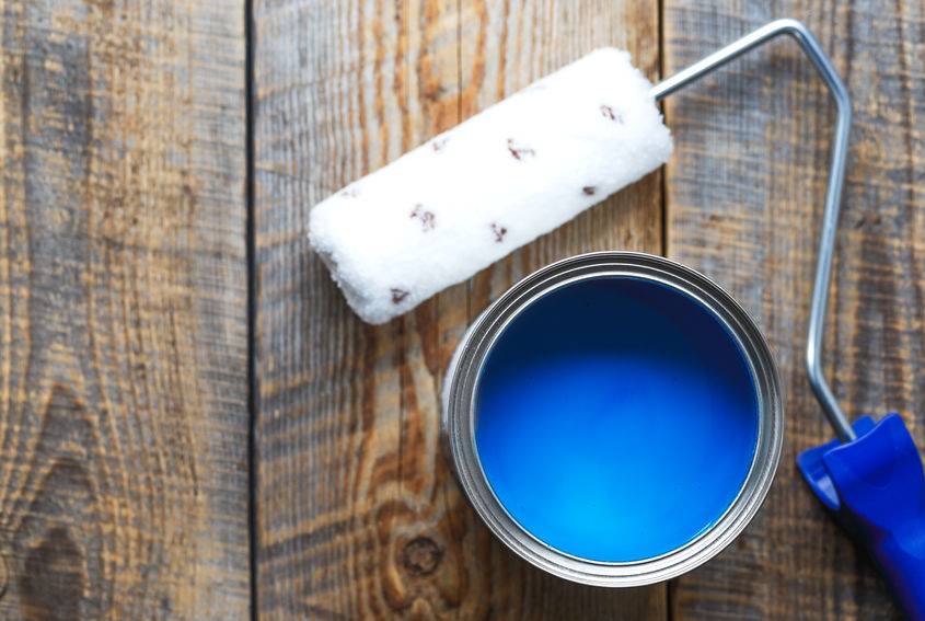 painting at home with can of blue paint with paint roller on wooden background top view